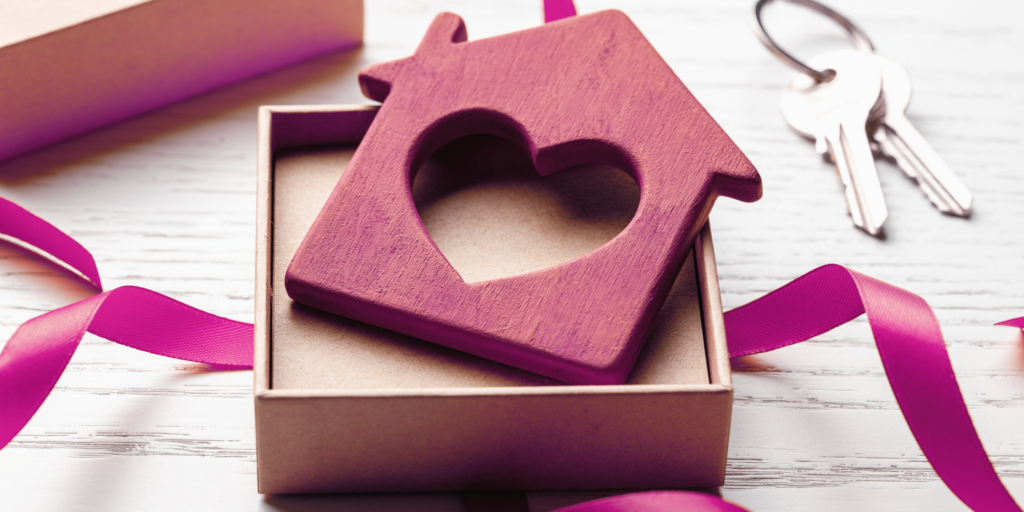 gift box holding a wooden house with a heart in the middle. keys next to box.